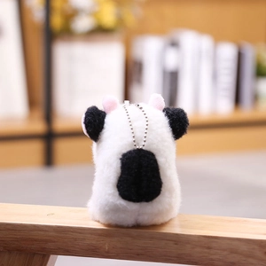Llavero de vaca de peluche suave con manchas negras y cadena de metal sobre madera