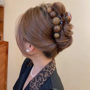 Detail view of large dark brown acrylic hair claw with amber round beads on hair