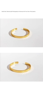 Dettaglio di un bracciale dorato aperto con trama a strisce verticali e riflessi di luce
