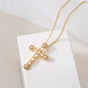Elegant gold cross pendant necklace with clear stones on a white jewelry display box