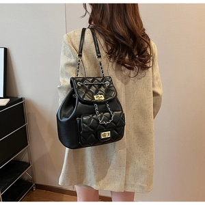 Detail of black quilted leather backpack with gold turn-lock and chain strap on model