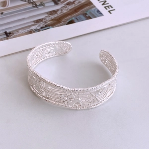 Detailed close-up of a silver-toned open cuff bracelet with a textured woven metal finish