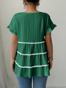 Detail view of the green layered short sleeve top with white tassel pom-pom trim on the back