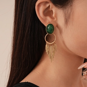 Detail view of vintage gold tassel earrings with dark green oval resin on a model