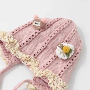 Pink knit baby winter hat with delicate lace trim and warm earflaps featuring soft chin straps