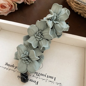 Détail de la barrette banane à fleurs en tissu gris-vert sur un plateau élégant