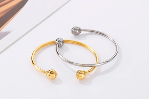 Close-up of gold and silver open cuff bracelets with spherical ends on white background