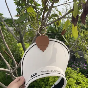 White sun visor hat with leaf-shaped brown leather magnetic clip and golden ring detail
