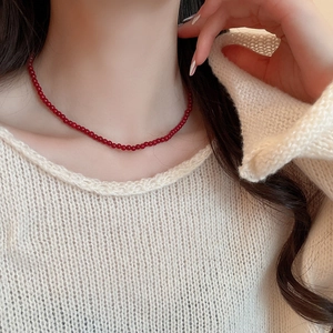 Detailed close-up of dark red garnet bead necklace worn over a white knitted sweater