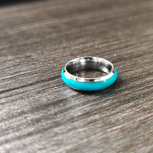 Glow-in-the-dark turquoise inlay on a polished stainless steel ring on wood base