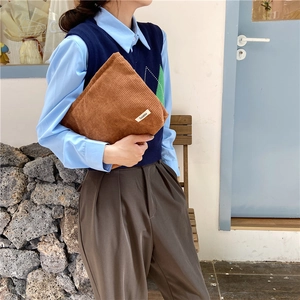 Caramel brown corduroy cosmetic bag held by a model in a minimalist lifestyle setting