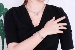 Close-up of elegant silver heart pendant necklace and matching bracelet on model