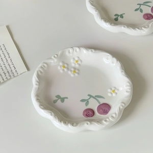 Detailed top view of white ceramic dessert plates with purple cherry patterns and wavy edges