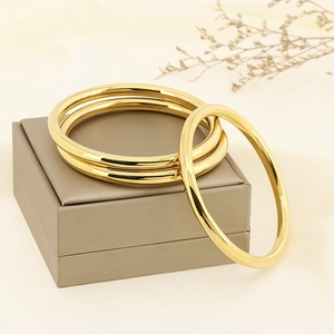 Three classic 6mm polished gold stainless steel bangles set on a warm elegant background