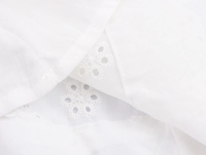 Detailed close-up of white midi dress featuring intricate floral embroidery and eyelet fabric