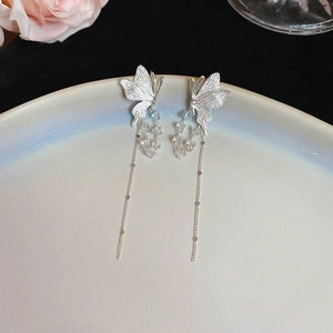 Detail of silver butterfly tassel earrings with crystal stones on a ceramic plate