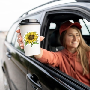 Sunflower vinyl sticker on a white coffee cup in a scenic outdoor setting