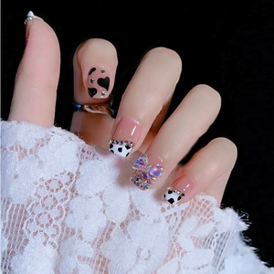 Press-on nails with cow print, 3D iridescent bows, and rhinestones on a model hand