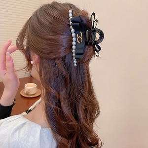 Detailed view of elegant black satin bow hair claw with pearls and gold metal emblem