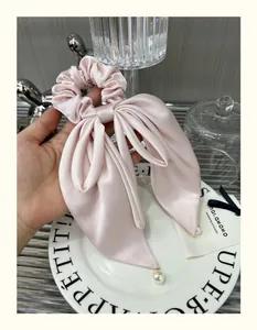 Close-up of pink satin hair scrunchie with large bow and elegant pearl pendant detail