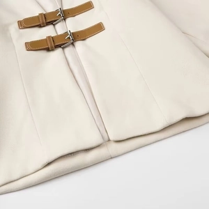 Close-up of cream soft jacket featuring brown leather strap and silver metal buckle