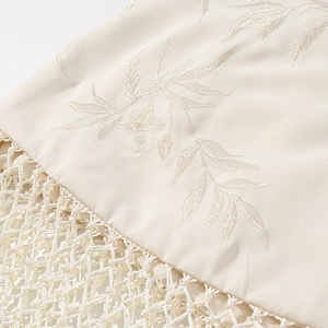 Détails de broderie de feuilles et franges en maille sur tissu de jupe couleur crème