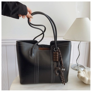 Detailed view of a black tote bag with white contrast stitching and cute charms