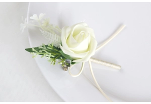Detailed view of cream PE rose boutonniere with green leaves and gold ribbon on plate