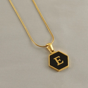 Detail of a gold snake chain necklace with a black hexagonal pendant featuring the letter E