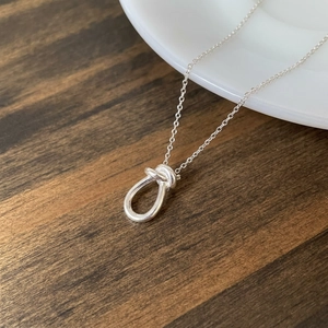 Minimalist 925 sterling silver knot pendant necklace displayed on a white ceramic cup