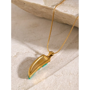 Detail of 18k gold plated necklace featuring a tusk pendant with green stone inlay on stone