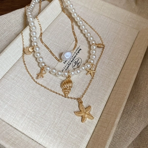 Detailed close-up of multilayer gold necklace with starfish charms and baroque pearls