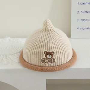 Close-up of baby knit hat featuring embroidered bear patch and rolled brim detail