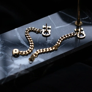 Detailed macro of gold plated letter C chain tassel earrings on marble background
