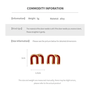 Macro detail of gold-plated alloy letter m earrings with red enamel and dimension specs
