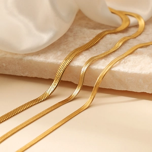 Three gold flat snake chain necklaces in various widths on white stone and silk fabric
