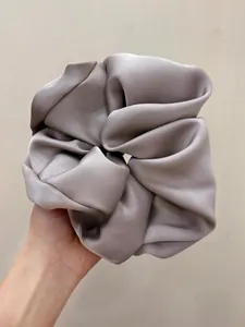 Detail shot of large silver satin scrunchie with glossy silk texture and pleated fabric