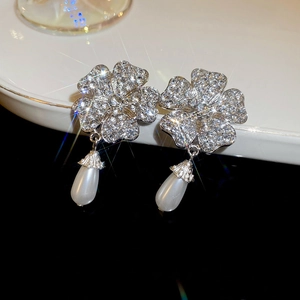 Macro detail of diamond floral earrings with elegant teardrop pearl charms in silver