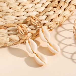 Detailed macro view of golden shell and natural conch seashell drop earrings on straw mat