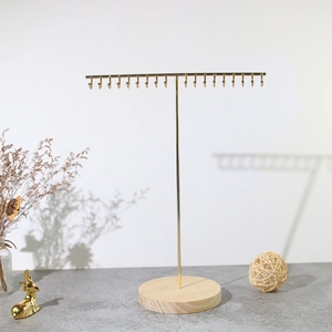Detail of golden T-bar jewelry stand with multi-hook design and round wooden base
