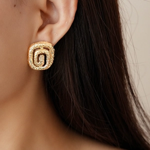 Close-up of golden geometric spiral earrings with hammered texture on a female model