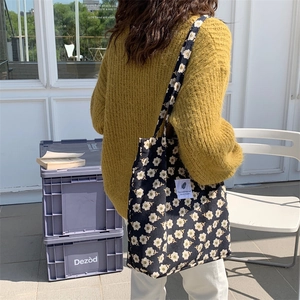 Outdoor shot of a black floral corduroy tote bag worn on a shoulder over a yellow sweater