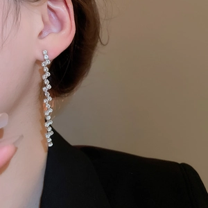 Macro shot of silver zircon tassel earrings with a chic wave design worn by a model