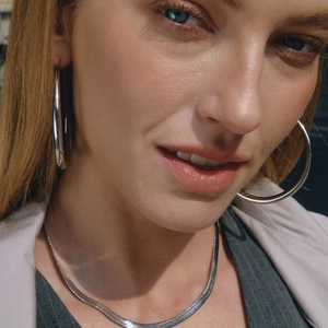 Close-up of polished stainless steel hoop earrings and flat snake chain necklace
