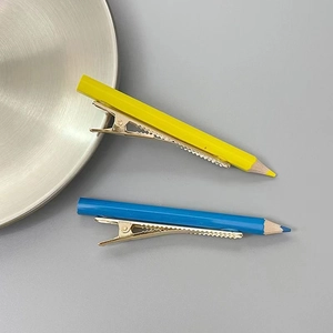 Détail de barrettes créatives en forme de crayon jaune et bleu sur base en métal doré