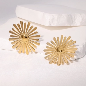 Elegant gold sunburst earrings in stainless steel on a white stone background