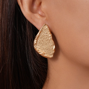 Close-up of gold geometric earrings with hammered texture on female model's ear