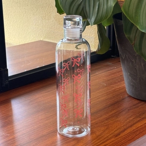 Close-up of a clear water bottle featuring a red bow design against a natural background
