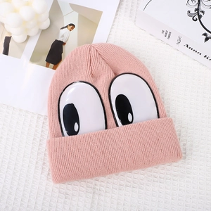 Pink knitted beanie hat for children with cartoon big eyes on a white grid background