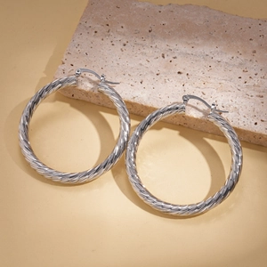 Close-up of large silver geometric spiral hoop earrings with a twisted metal texture